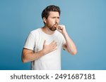 Portrait of young sick man coughing on blue background in studio. Health care, medicine concept