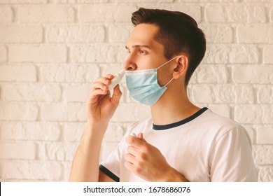 Portrait Of Young Sick Man Using Nasal Drops For Runny Congested Nose. Confident Sick Doctor In Medical Protective Mask On Face Using Nose Spray. Pandemic Coronavirus COVID-19 NCov-19 Symptoms