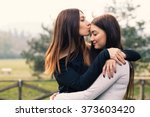 Portrait of young sisters hugging and kissing outdoors in a park. 