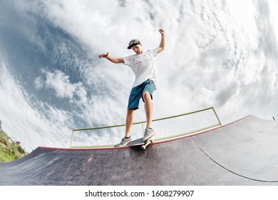 Portrait of a young skateboarder doing a trick on his skateboard on a halfpipe ramp in a skate park in the summer on a sunny day. The concept of youth culture of leisure and sports