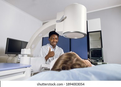 Portrait of young smiling African American man doctor, looking at camera with thumb up, while providing lithotripsy procedure for his female patient with modern ultrasonic lithotriptor