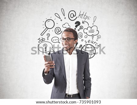 Portrait of a young smiling African American businessman wearing a suit and a shirt and looking at his smartphone screen. Gray background, internet search