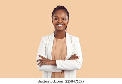 Portrait of young smiling african woman standing with folded arms and looking at camera. Confident stylish business woman in blouse and jacket standing on beige background with copy space. Banner. - Powered by Shutterstock