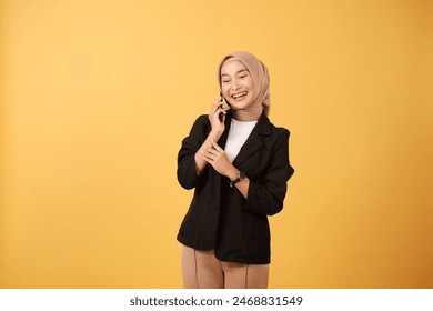 Portrait of young smiling Asian hijab woman with black coat talking on smartphone isolated on yellow background, Asian Thai Indonesian model - Powered by Shutterstock