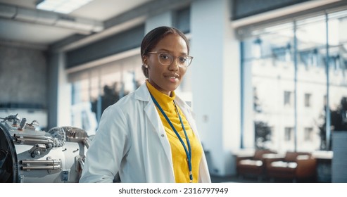Portrait of Young Smiling Black Woman Wearing Glasses and a Lab Coat Looking at the Camera. Future Engineer Pursuing Scientific Career. Industrial Manufacturing Student in University Laboratory Posing