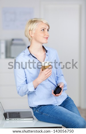 Portrait of a young smiling businesswoman with coffee cup looking up at office desk