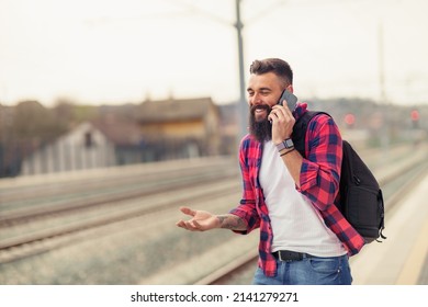 Portrait Of Young Smiling Caucasian Man Speaking On Mobile Phone At Train Station.