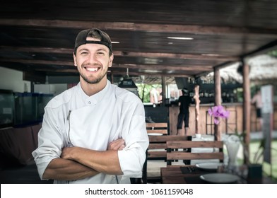 Portrait of a young smiling chef standing on the background of a summer restaurant - Powered by Shutterstock