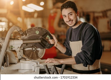 Portrait Of Young Smiling Confident Carpenter At Work Place, Handsome Caucasian Craftman Love Cutting Wood, Work In Factory