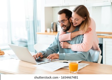 Porträt von jungen lächelnden Paaren während der Arbeit mit Laptop und Dokumente in der gemütlichen Küche zu Hause