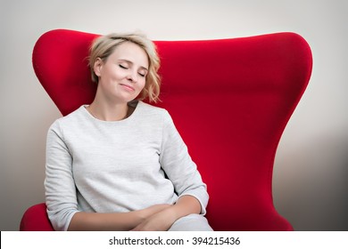 portrait of young smiling, dreaming woman sitting in armchair