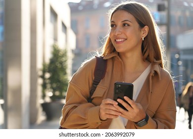 Portrait of young smiling fashion woman wearing coat holds smartphone looking through shop window on city street. Copy space. - Powered by Shutterstock