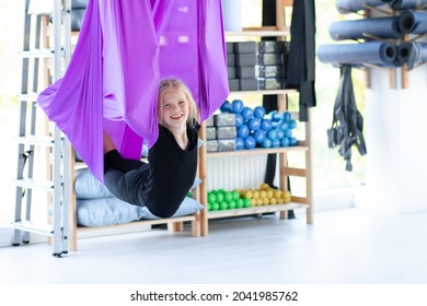 Portrait young smiling girl practice in aero stretching swing in purple hammock in fitness club. kids Aerial flying yoga exercises.