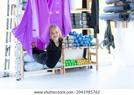 Portrait young smiling girl practice in aero stretching swing in purple hammock in fitness club. kids Aerial flying yoga exercises.