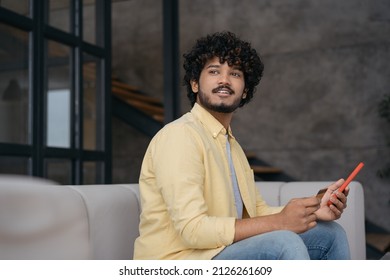 Portrait Of Young Smiling Indian Man Holding Credit Card Using Mobile Phone Shopping Online. Mobile Banking. Handsome Asian Guy Ordering Food Online Looking Away Sitting At Home, Copy Space