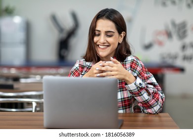 Portrait Of A Young Smiling Indian Woman Working On Her Laptop, Sitting In An Office Cafeteria, Coffee Shop, Casual Work Environment.