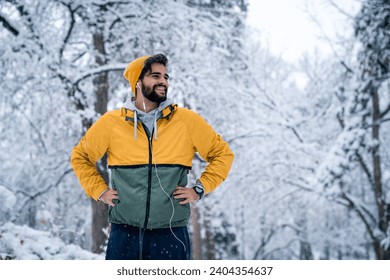 Portrait of young smiling man runner standing with hands on hips looking away during cold snowy day. - Powered by Shutterstock