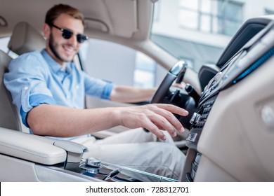 Portrait Of Young Smiling Man In Sunglasses Driving Car And Switching Radio