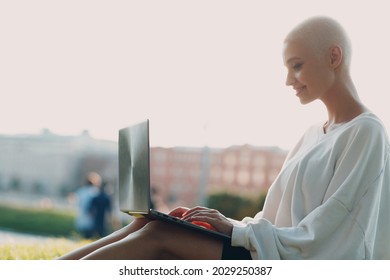 Portrait Of Young Smiling Millenial European Short Haired Woman Using Laptop At Green Grass Meadow In Park. Beautiful Happy Blonde Girl Outdoor. Summer Fashion Female Clothing.