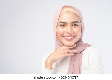 A portrait of young smiling muslim woman wearing a pink hijab over white background studio.