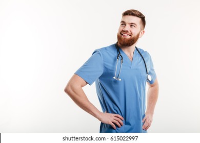 Portrait Of A Young Smiling Positive Man Doctor With Stethoscope Holding Hands On Hips And Looking Away Isolated On A White Background