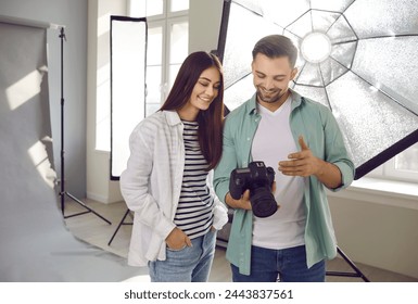 Portrait of a young smiling professional photographer showing photos to a girl model on digital camera standing in production studio with light equipment and discussing photo session. - Powered by Shutterstock