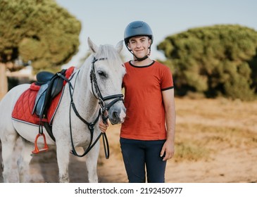 portrait of young smiling rider standing next to his white horse in a pine grove - Shutterstock ID 2192450977