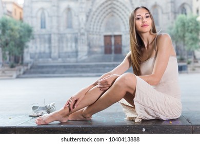 portrait of young smiling swedish adult girl in evening  apparel sitting  with sandals in european town