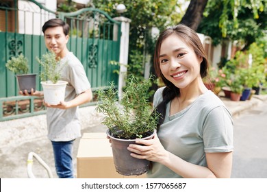 Portrait of young smiling Vietnamese woman posing with potted flower when moving in new house with her boyfriend - Shutterstock ID 1577065687