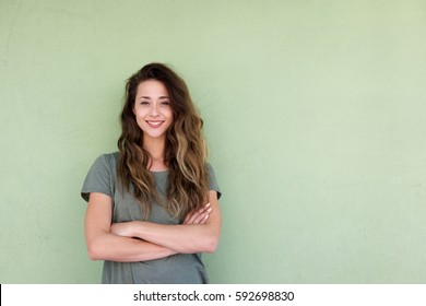 Portrait Of Young Smiling Woman With Arms Crossed Against Green Background