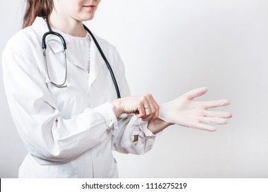 Portrait of young smiling woman brunette doctor in glasses and medical white coat with stethoscope putting on disposable medical gloves on white background - Powered by Shutterstock