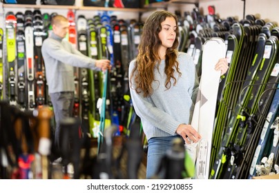 Portrait Of Young Smiling Woman Choosing New Skis In Shop Of Sports Equipment