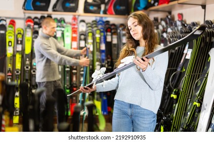 Portrait Of Young Smiling Woman Choosing New Skis In Shop Of Sports Equipment