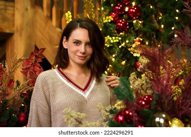 Portrait Young Smiling Woman In Cozy Sweater Against Backdrop Of Christmas Decorations At Home. Girl Celebrates Christmas And New Year In Festive Home Atmosphere