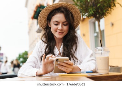 Portrait of young smiling woman drinking using cellphone while drinking milkshake in cozy cafe outdoors - Shutterstock ID 1766690561