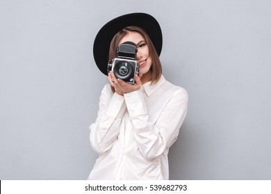 Portrait of a young smiling woman filming with retro camera isolated on the gray background