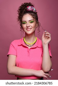 Portrait of young smiling woman on pink background. Female with unusual green eyes shadows makeup, curly hair and earrings. - Shutterstock ID 2184306785