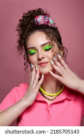 Portrait of young smiling woman on pink background. Female with unusual green eyes shadows makeup, curly hair and earrings. Eyes closed. Hands are near face. - Shutterstock ID 2185705143