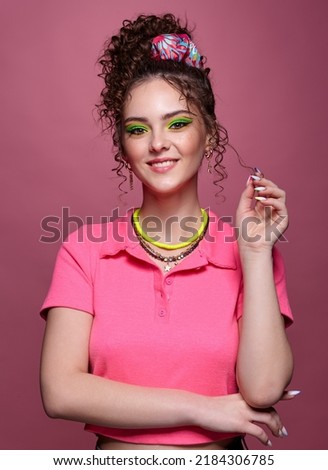 Portrait of young smiling woman on pink background. Female with unusual green eyes shadows makeup, curly hair and earrings.