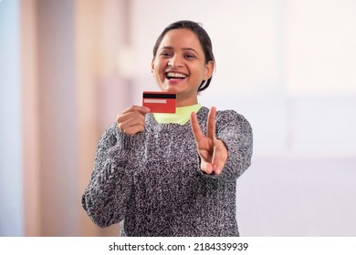Portrait of young smiling woman showing blank credit card and Victory