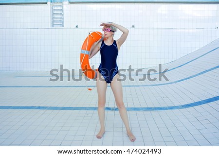 portrait of young smiling woman in swimsuit and swimming goggles standing with Lifebuoy in the empty swimming pool and looking for water