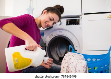 Portrait of the young smiling woman who sitting near washing machine in the room and pouring rinses into the lid - Shutterstock ID 787848499