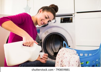 Portrait of the young smiling woman who sitting near washing machine in the room and pouring rinses into the lid - Shutterstock ID 790859881