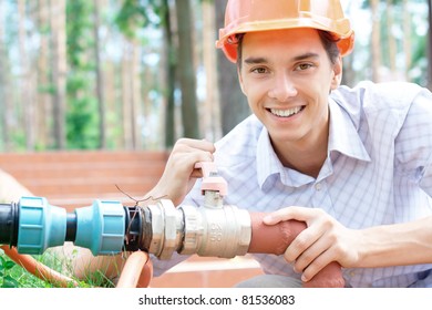 Portrait of a young smiling worker repairing a pipe outdoors with copy space