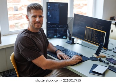 Portrait Of Young Software Engineer Looking At Camera While Writing Code At Workplace With Multiple Computer Screens