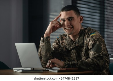 Portrait of a young soldier in a military uniform working on a laptop while sitting at a table at home. - Powered by Shutterstock