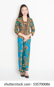 Portrait Of Young Southeast Asian Woman In Traditional Malay Batik Kebaya Dress Smiling, Full Body Standing On Plain Background.