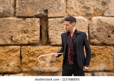 Portrait of young Spanish man in black shirt, jacket and pants, with black handkerchief with red polka dots and walking stick posing next to a stone wall. Flamenco concept, art, dance, culture. - Powered by Shutterstock