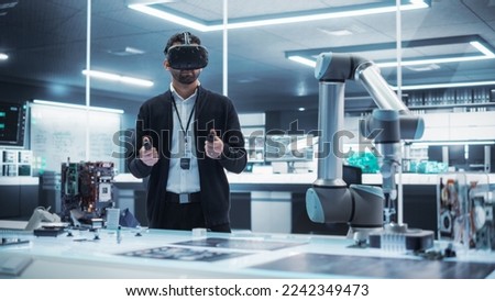 Portrait of a Young Specialist Using a Virtual Reality Headset with Controllers to Operate an Experimental Robotic Arm Machine. High Tech Industrial Laboratory Facility.