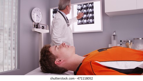 Portrait Of Young Sports Athlete Lying Down While Doctor Reviews Xrays.